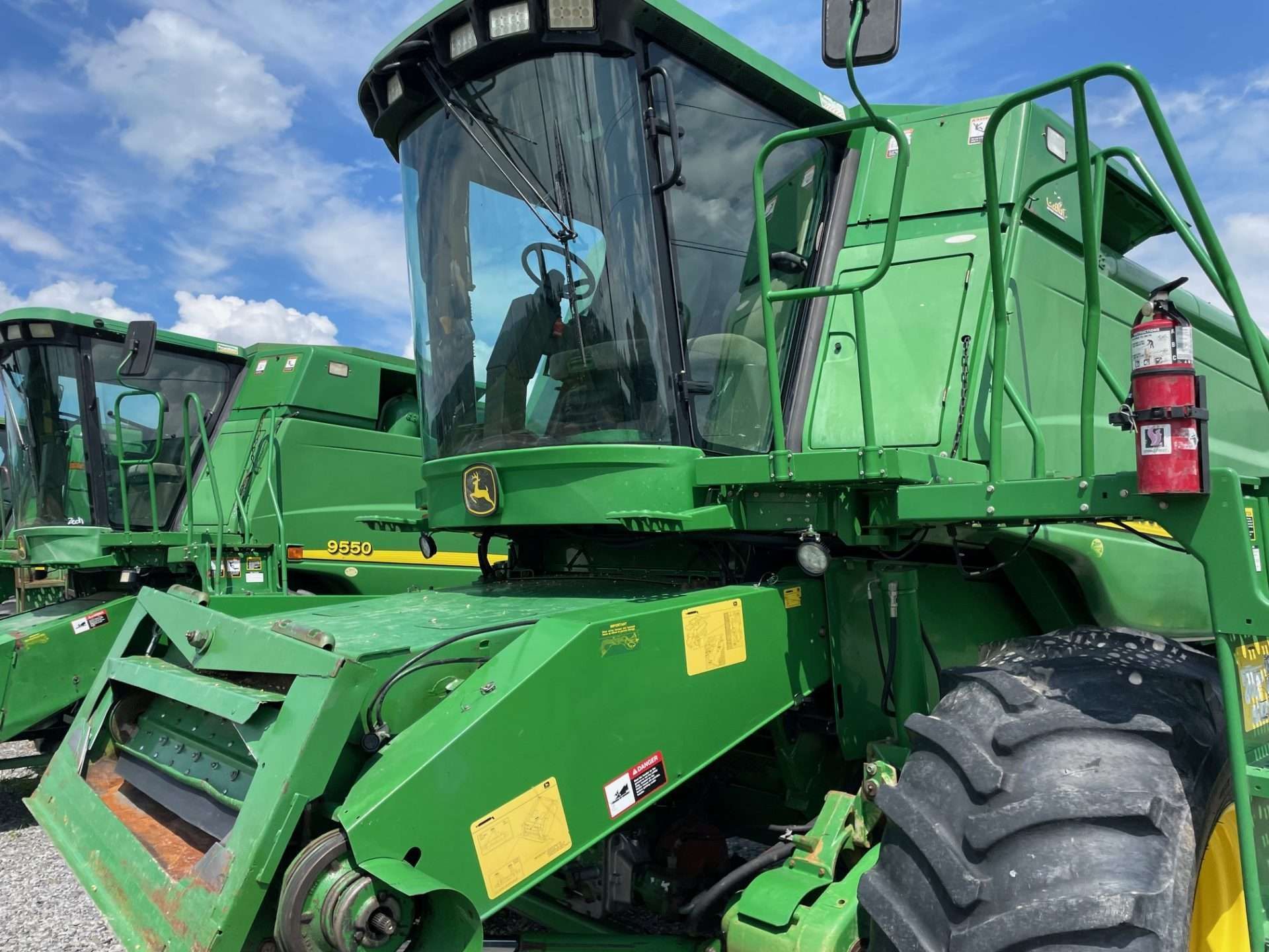 Green combine harvester in a field under a blue sky, with another machine behind it