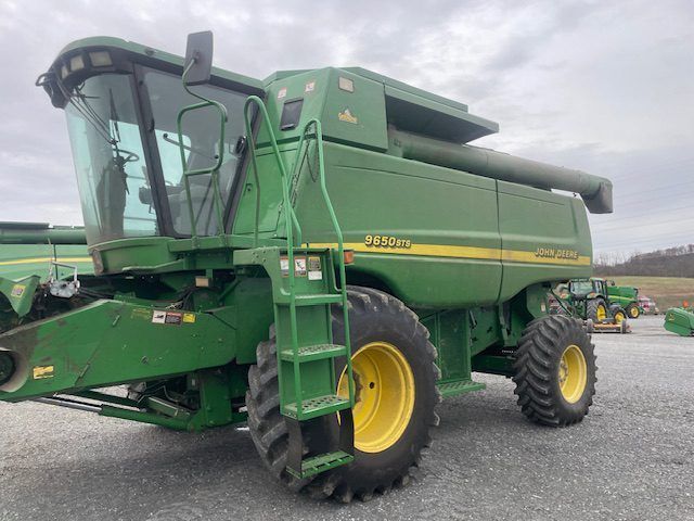 Green John Deere combine harvester parked on gravel under a cloudy sky