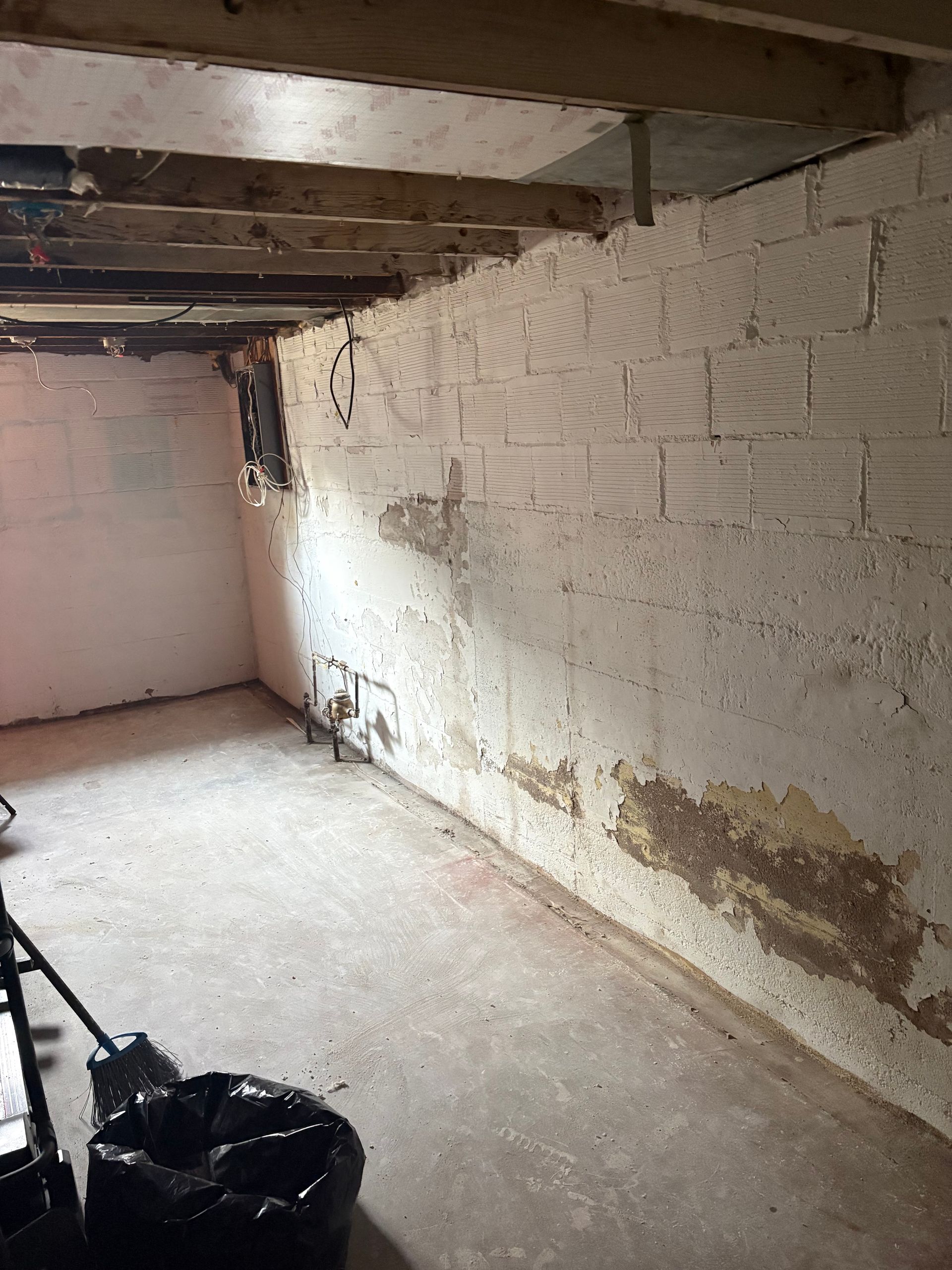 Empty basement room with white brick walls, exposed ceiling beams, and a concrete floor.
