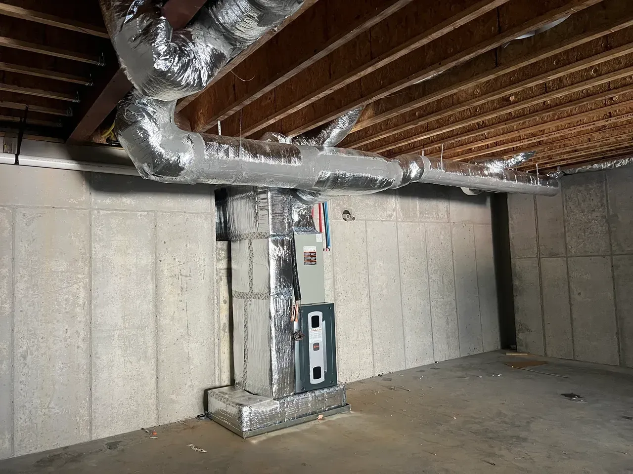 A basement with a furnace and ducts hanging from the ceiling.