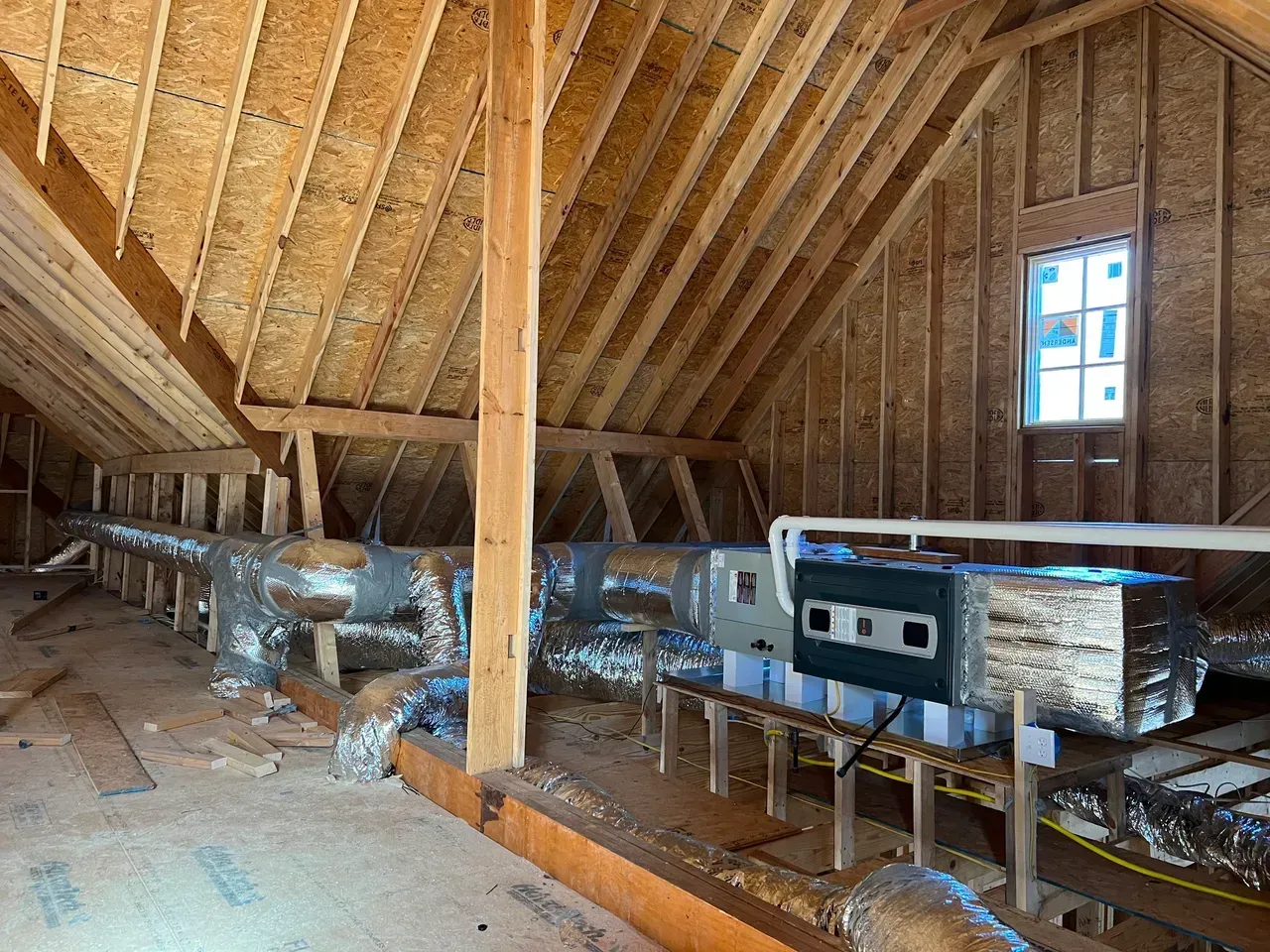The attic of a house under construction with a lot of pipes and ducts.