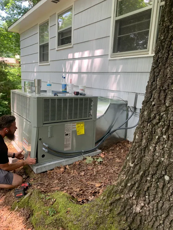 A man is working on an air conditioner outside of a house.