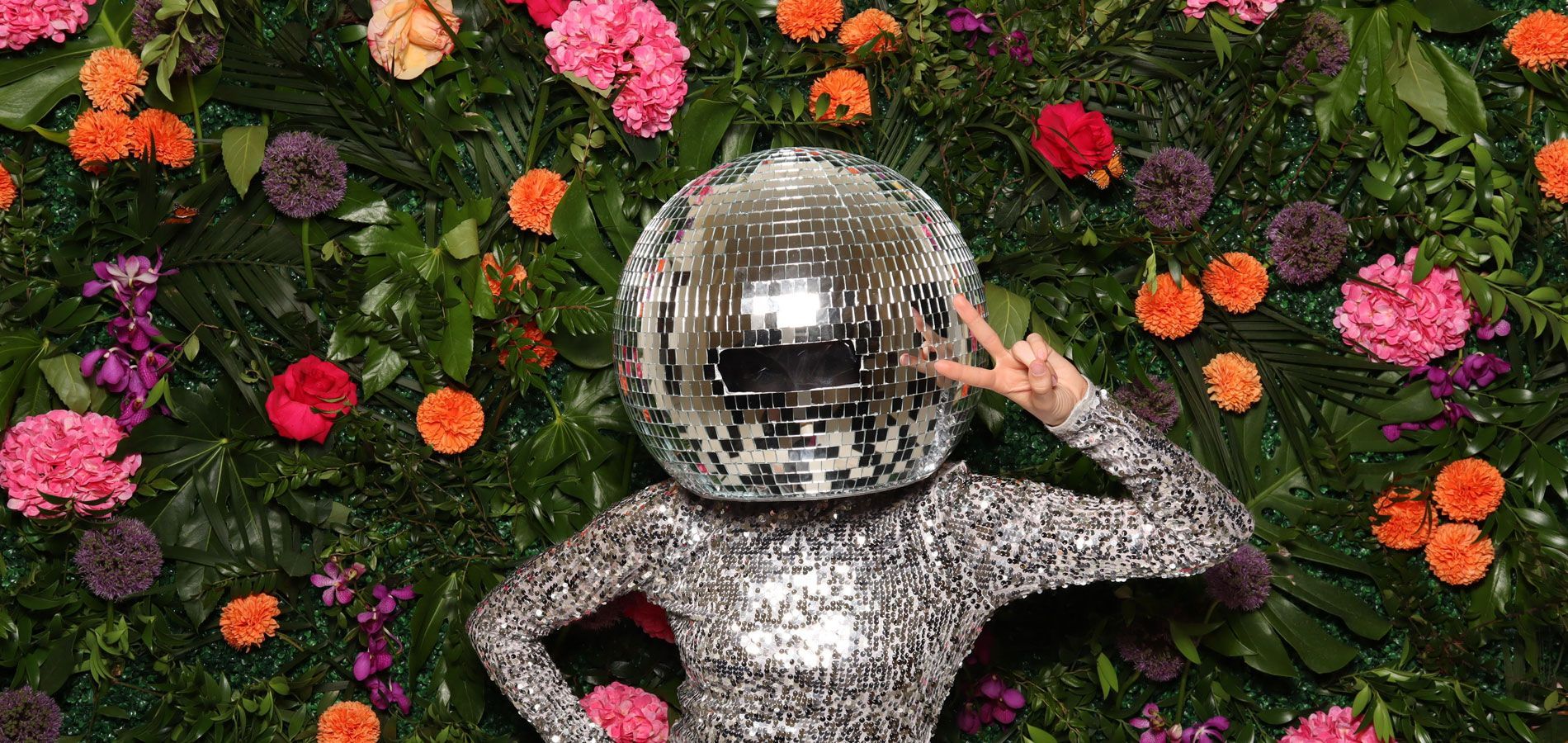 A woman with a disco ball on her head is surrounded by flowers