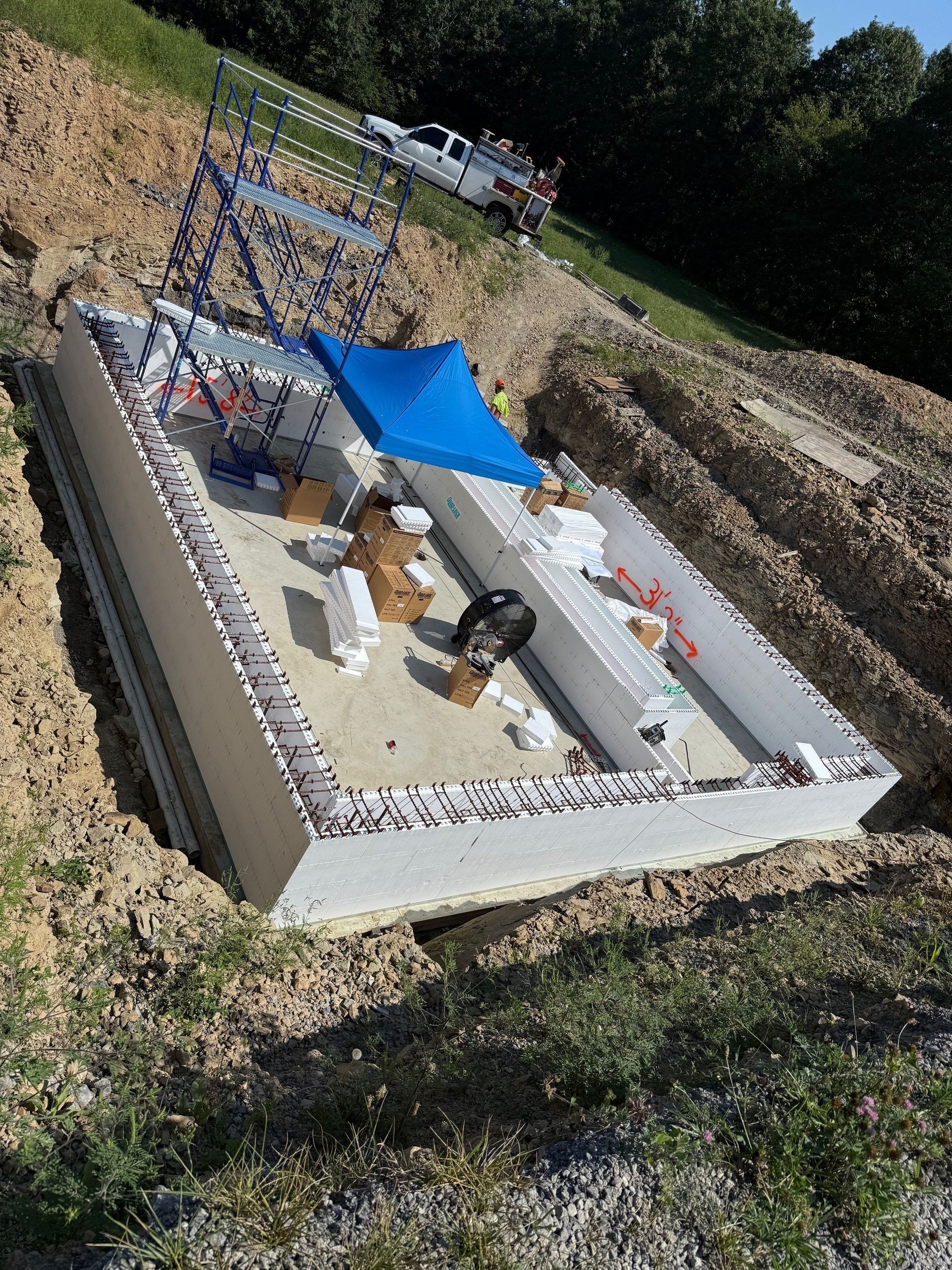 Construction site with a partially built concrete structure, a truck, and scaffolding on a hillside.