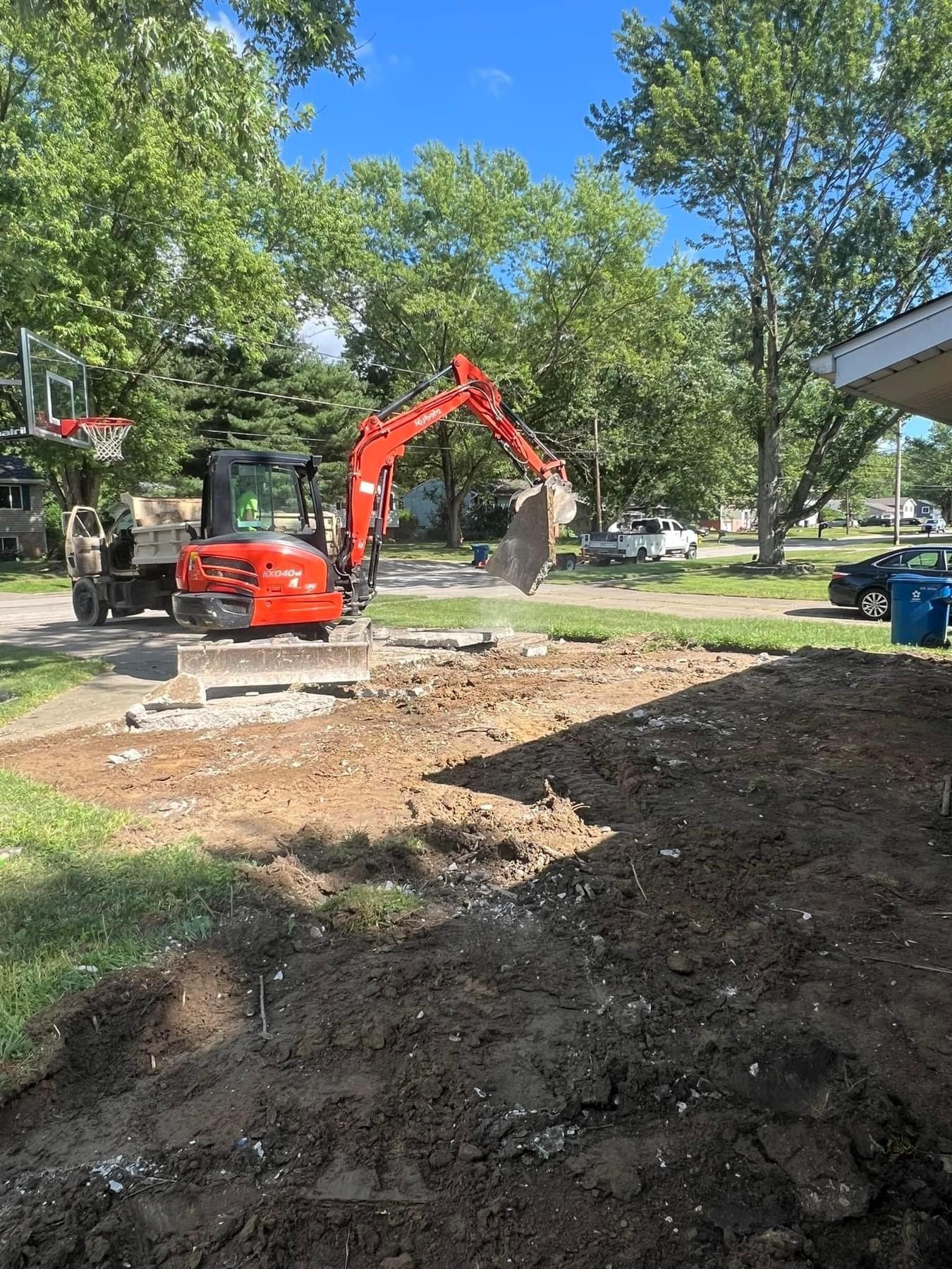 A red excavator is digging a hole in the dirt in front of a house