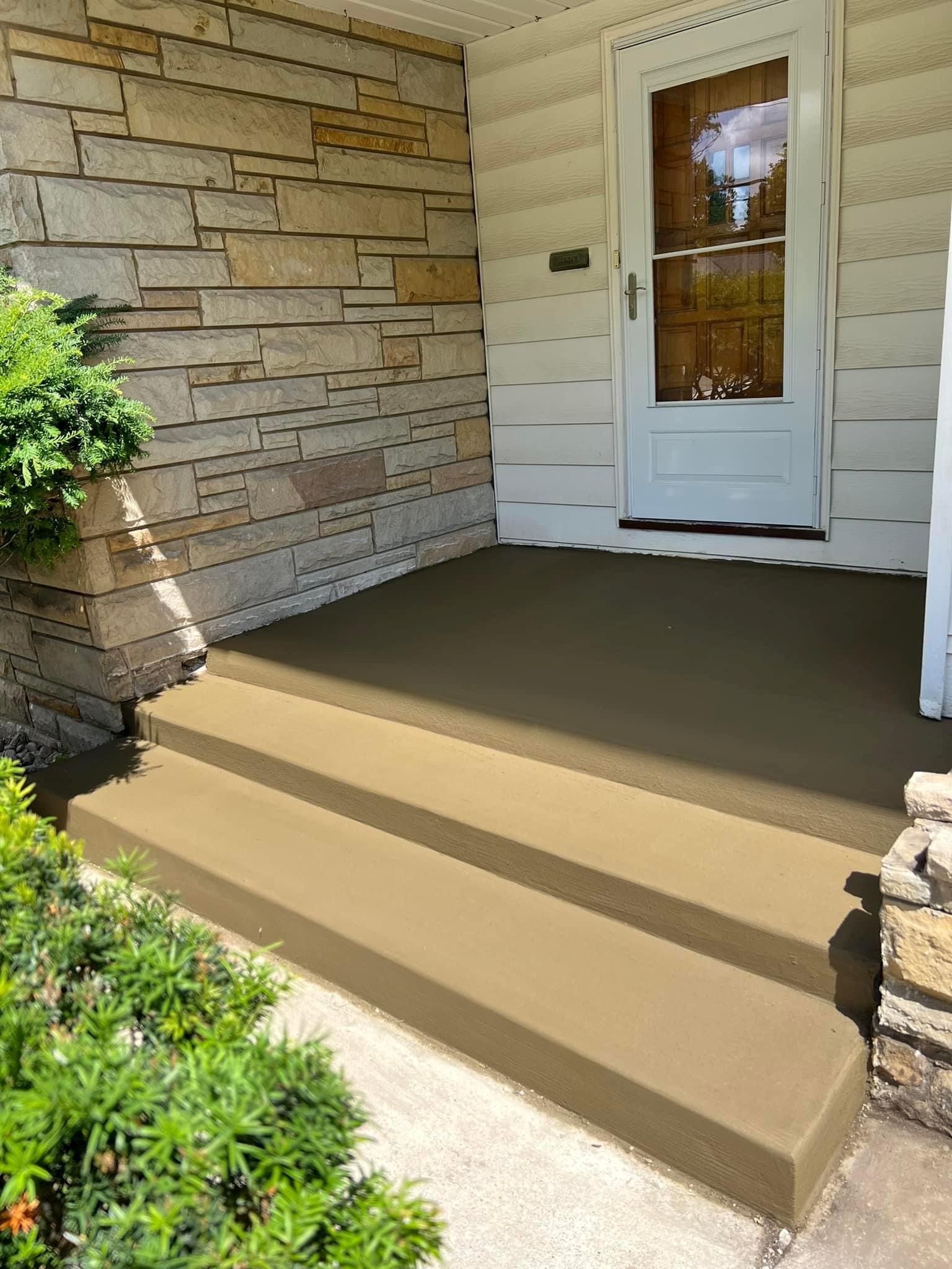 The front porch of a house with concrete steps and a stone wall
