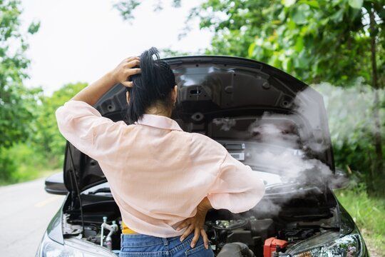 A woman is standing next to a broken down car with the hood open.