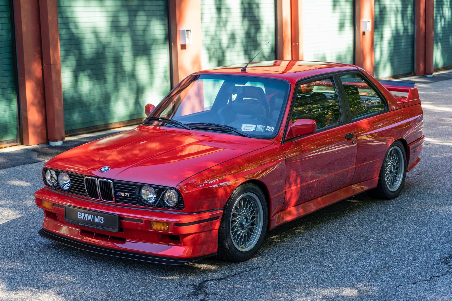 A red bmw e30 m3 is parked in front of a garage.