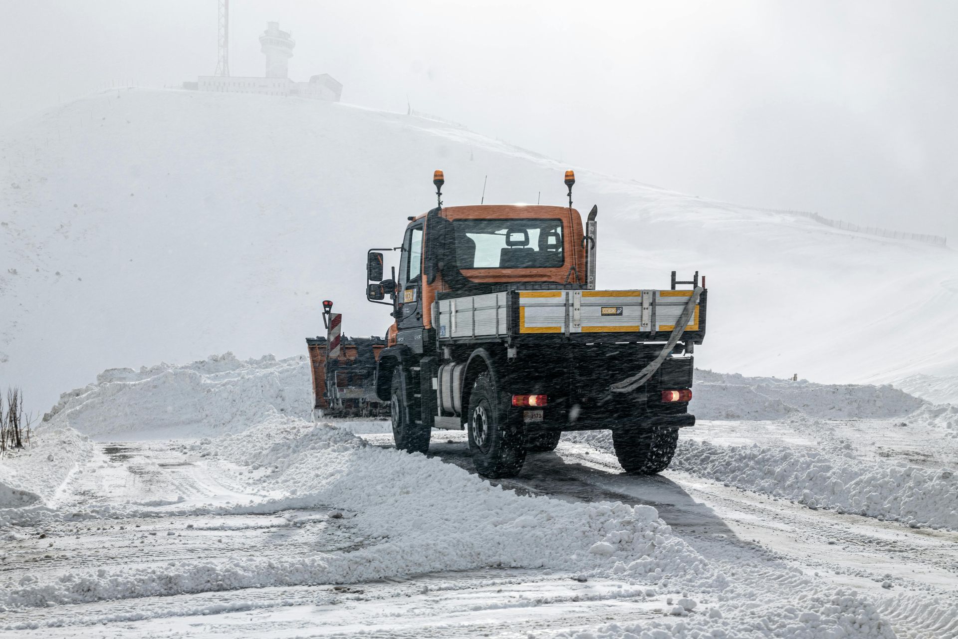 A snow plow is driving down a snow covered road.