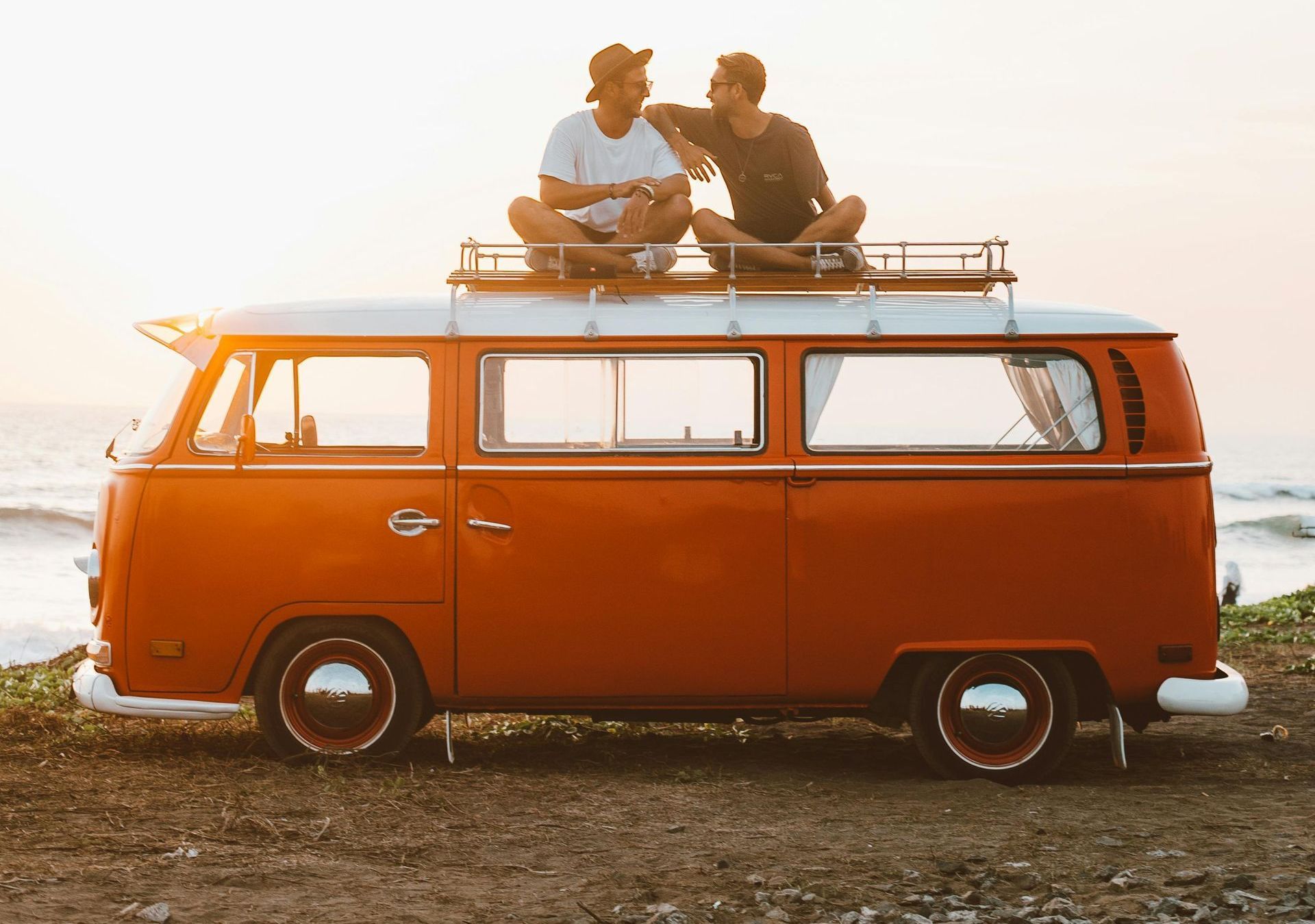 Two men are sitting on the roof of a red van.