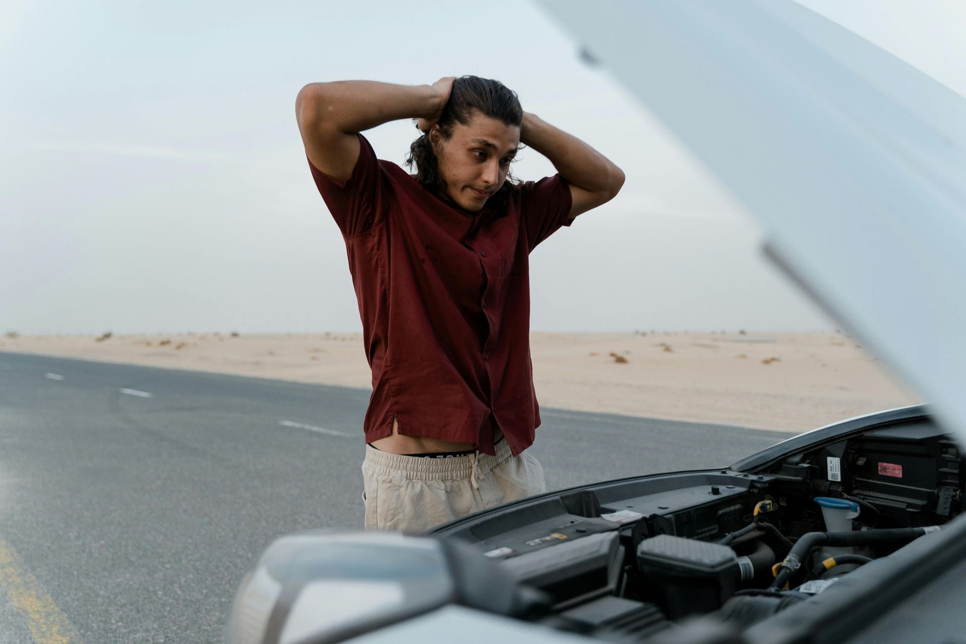 A woman is standing next to a broken down car with the hood open.
