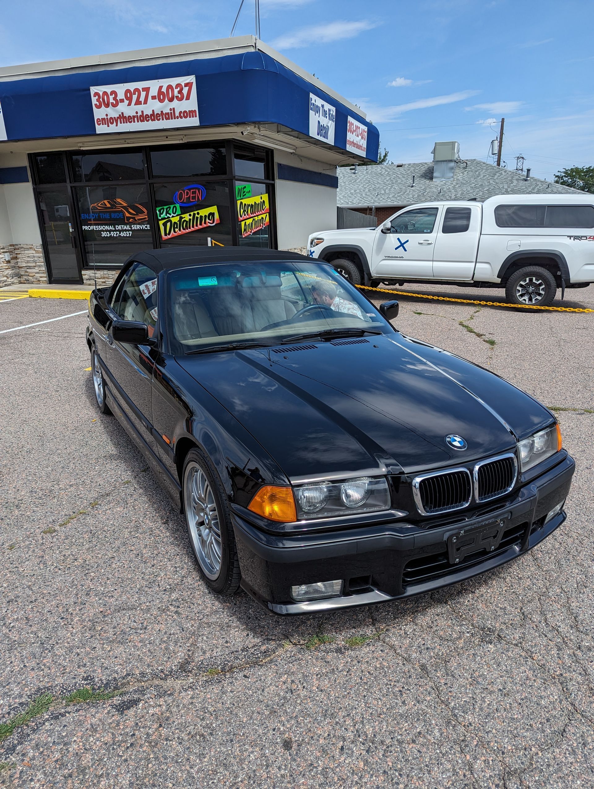 A black bmw convertible is parked in front of a car dealership.