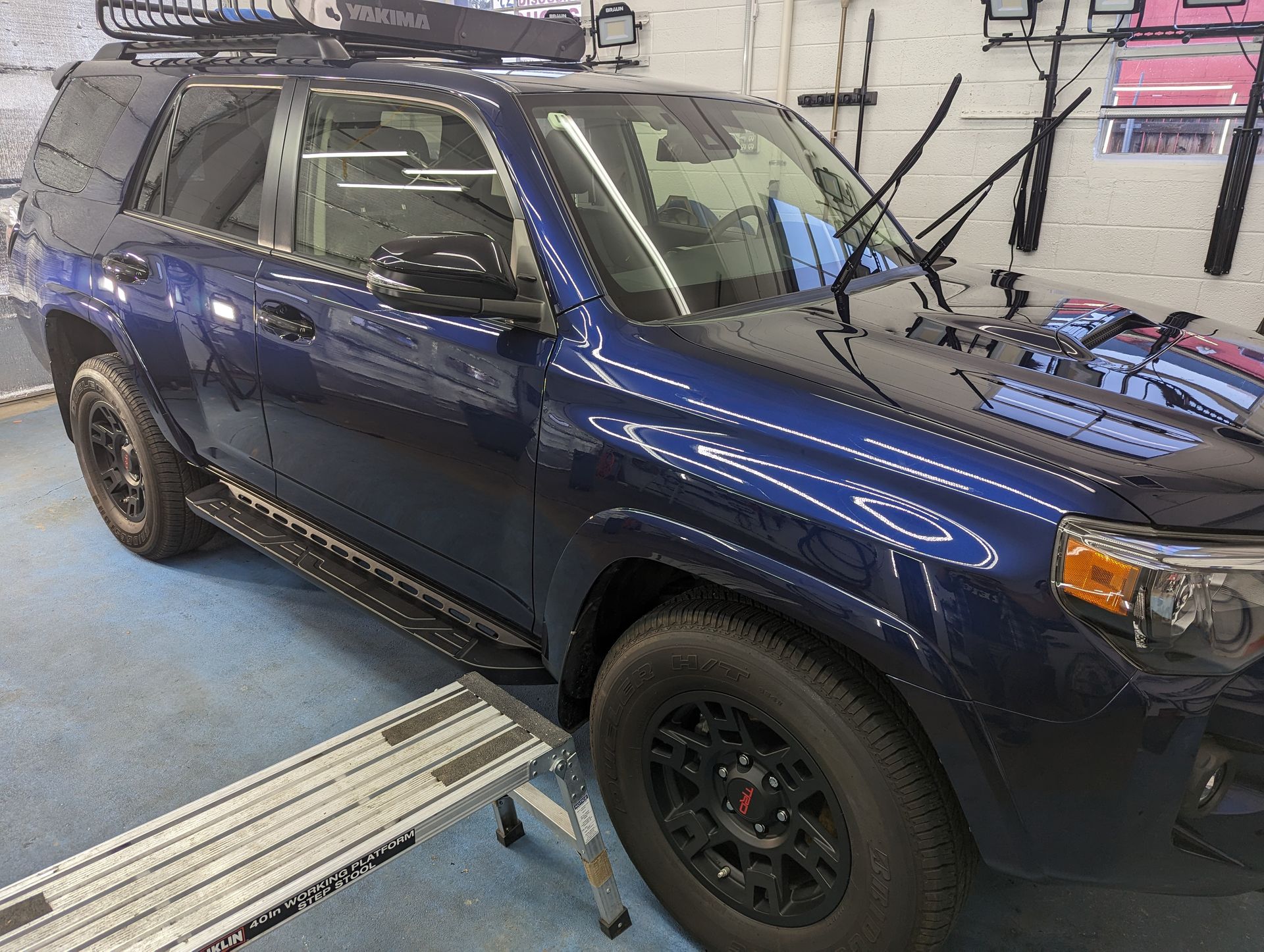 A blue suv is parked in a garage next to a ladder.