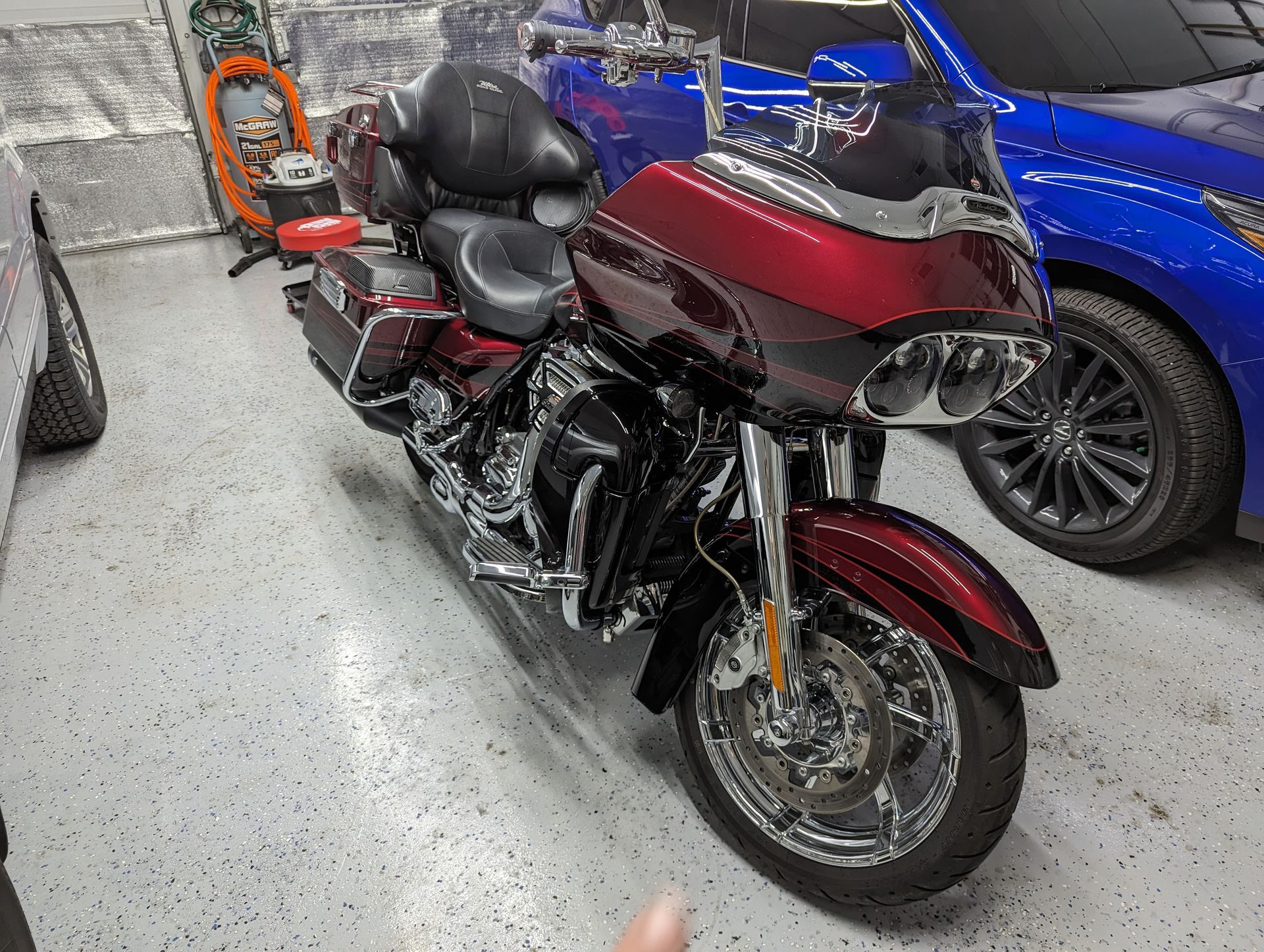 A red motorcycle is parked in a garage next to a blue car.
