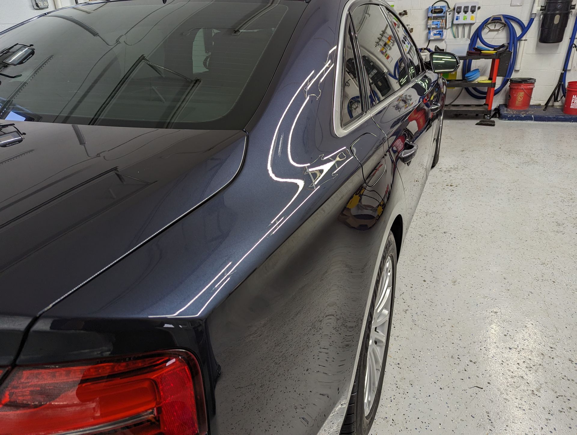 A black car is parked in a garage next to a vacuum cleaner