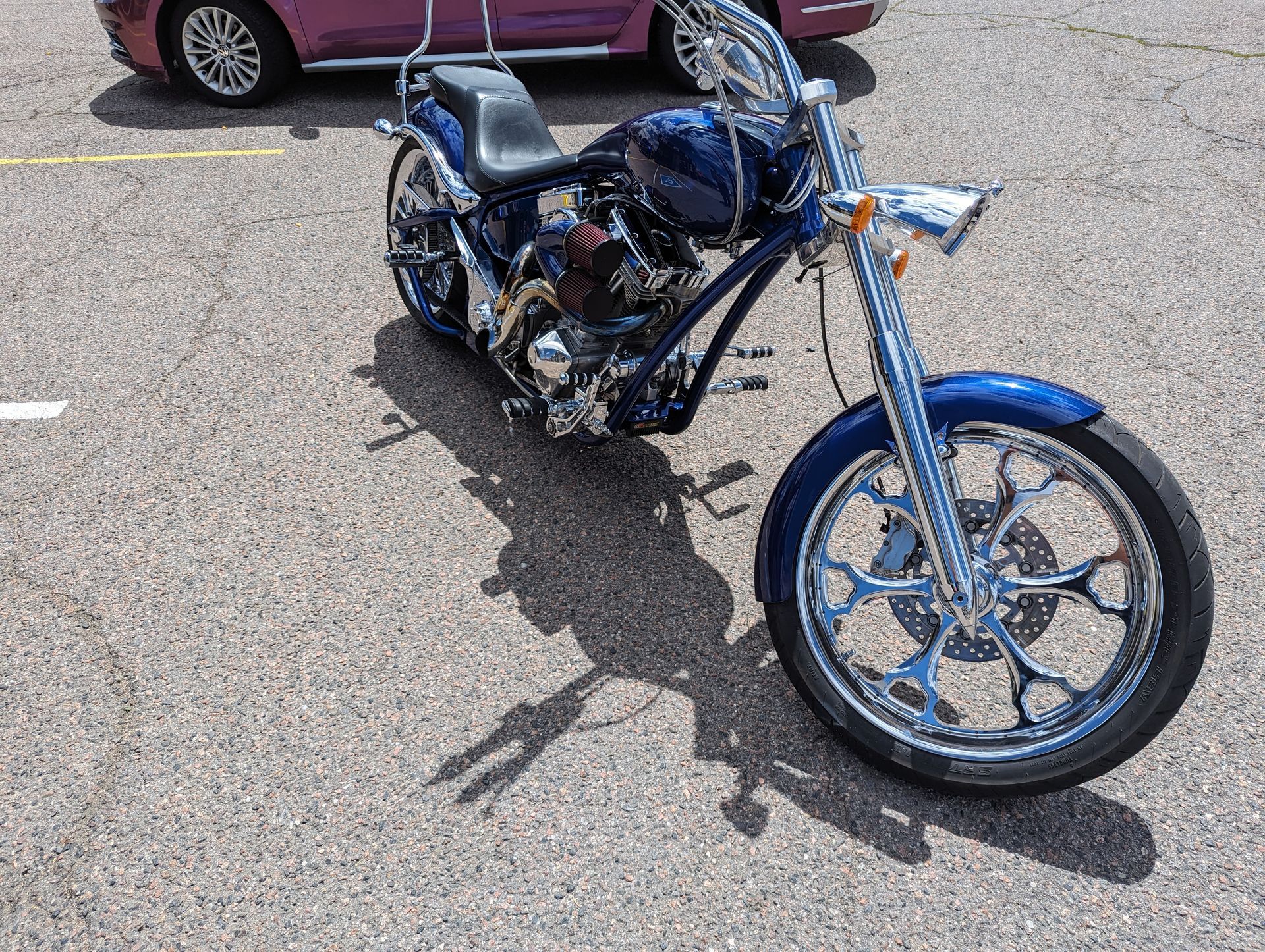 A blue motorcycle is parked in a parking lot next to a pink car.