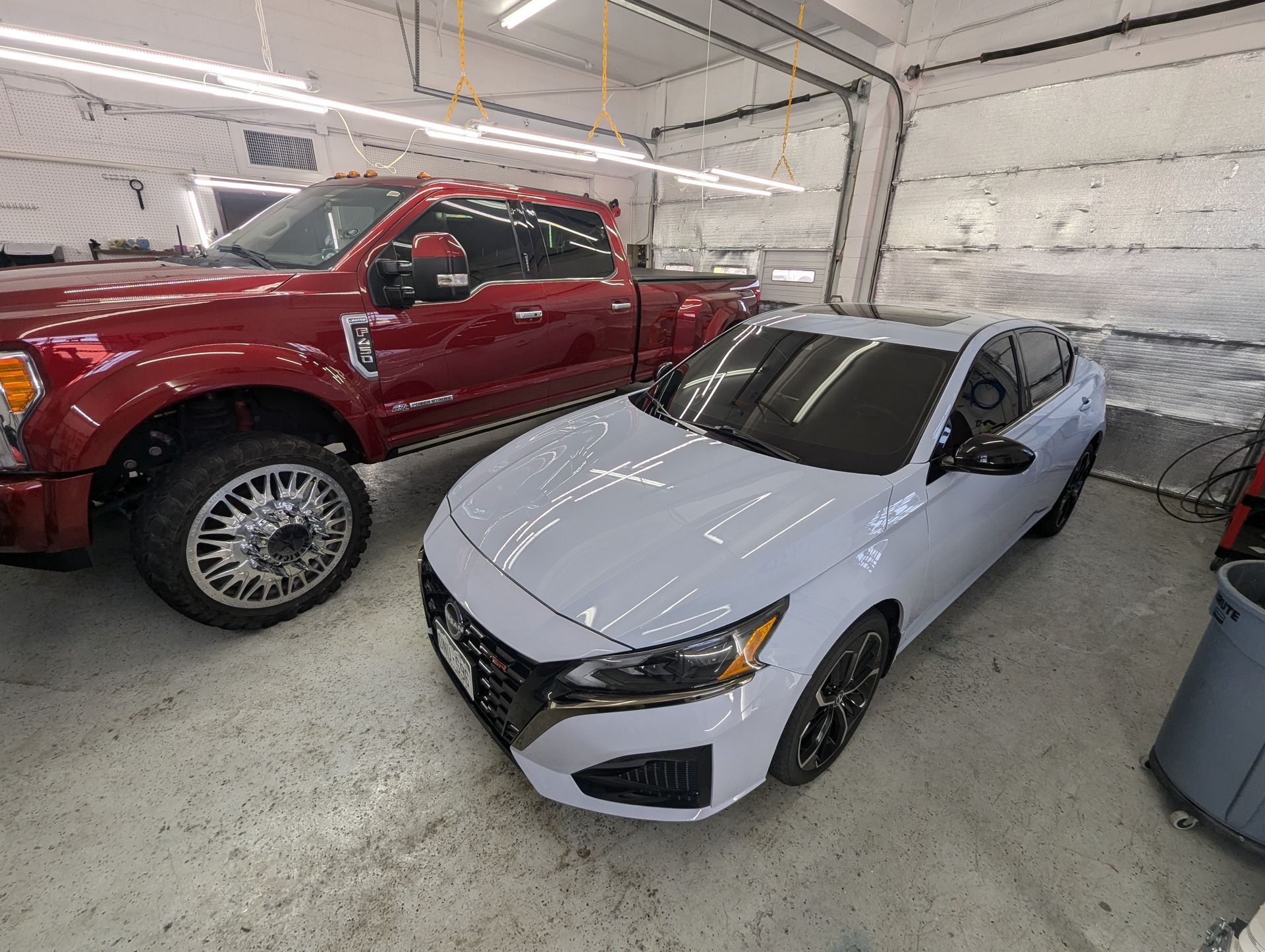A white car is parked next to a red truck in a garage.