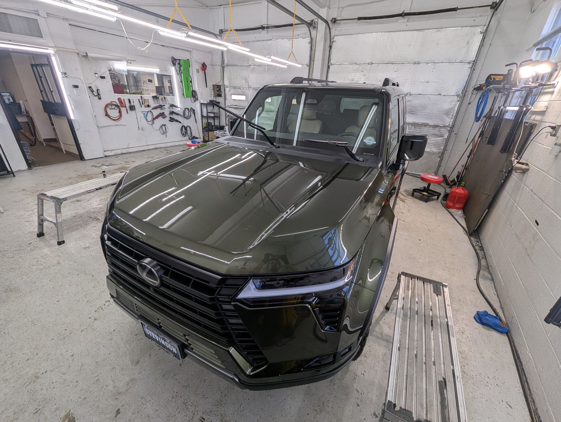 A green car is parked in a garage next to a ladder.