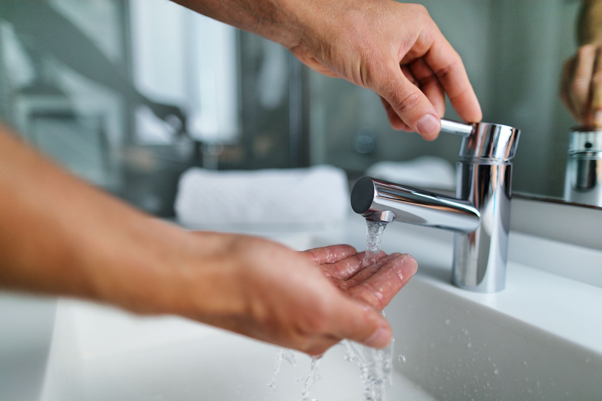 A person turning on a bathroom sink faucet with one hand and cupping the water with their other hand.