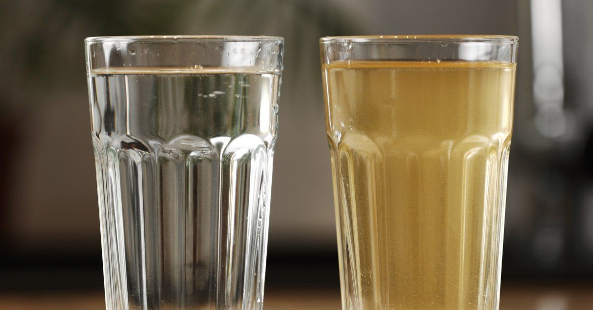 Two drinking glasses side by side on a table. One has clear, drinkable water and the other holds discolored dirty water.