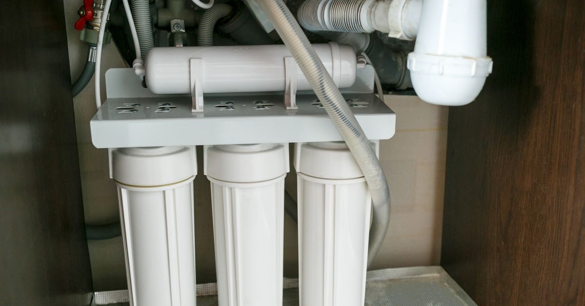 A reverse osmosis water filtration system connected to water pipes within a brown wooden cupboard.