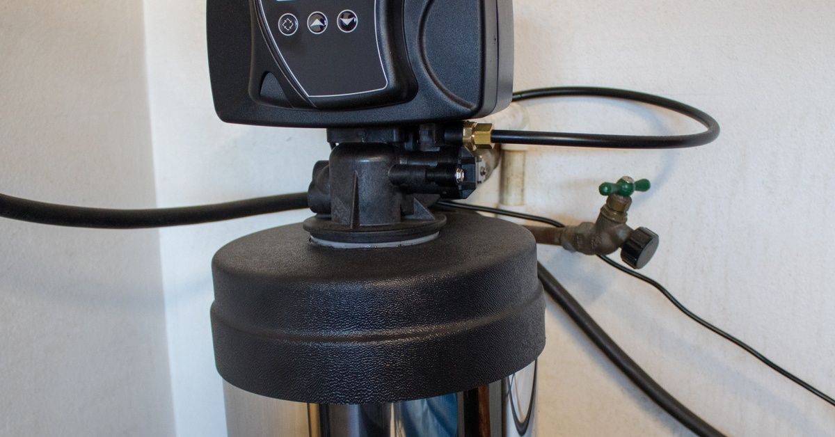 The top part of a water softener system, including the top of the tank, a control display, and hoses