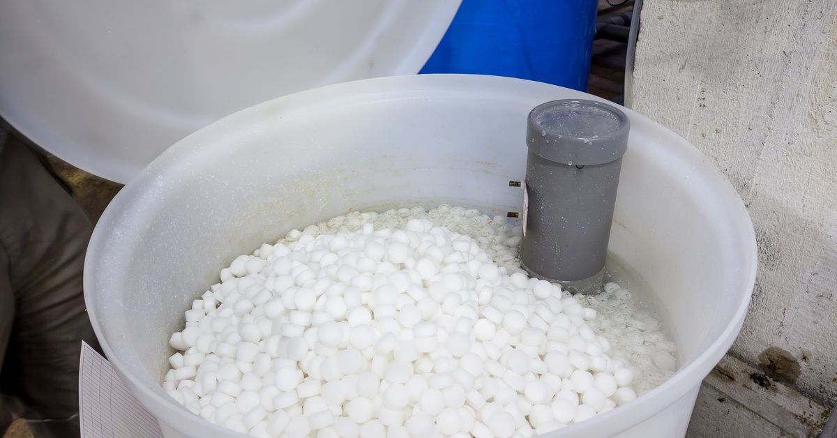 A white plastic tank full of salt pellets for a water softener system. The lid is open.