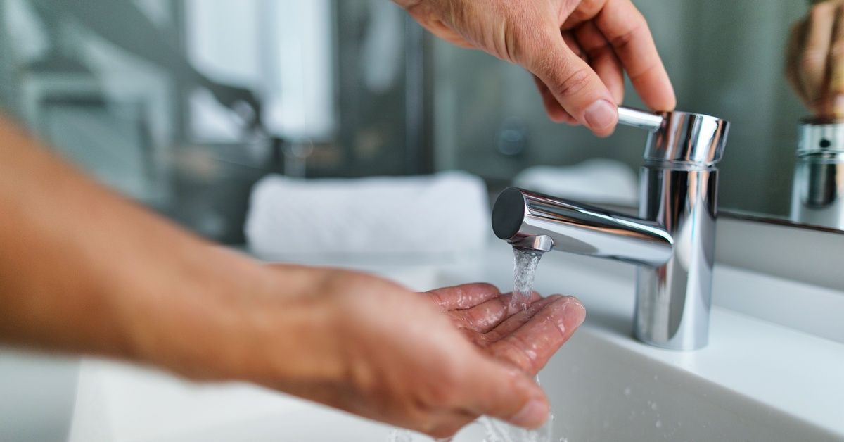 A hand turns on a sink faucet, while the other hand is held under the running water.
