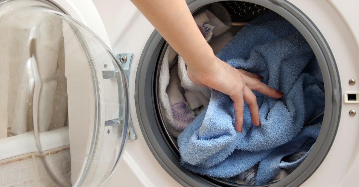 A hand inserts a blue towel into a dryer already containing a mix of different colored towels.