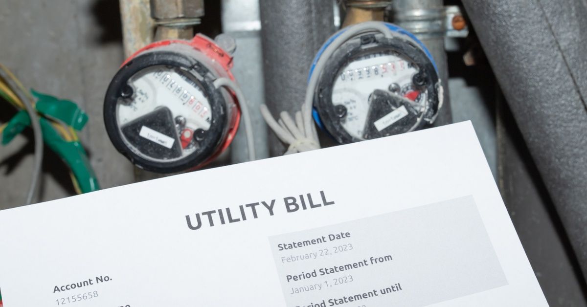 A paper utility bill held in front of a water heater with visible pipes and dials.