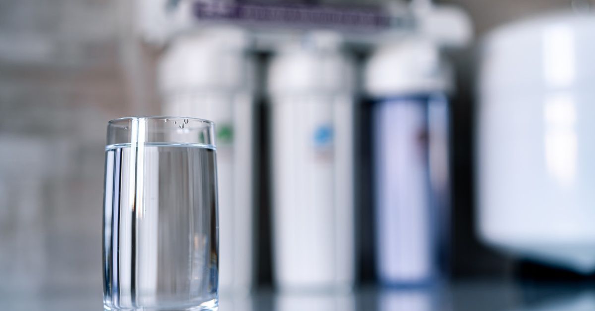 A glass of water on a counter, with a water purification system in the background.