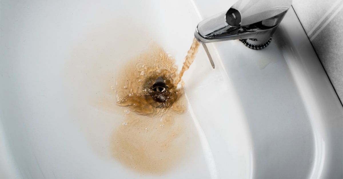 An overhead view of a sink, with brown water pouring from the tap.