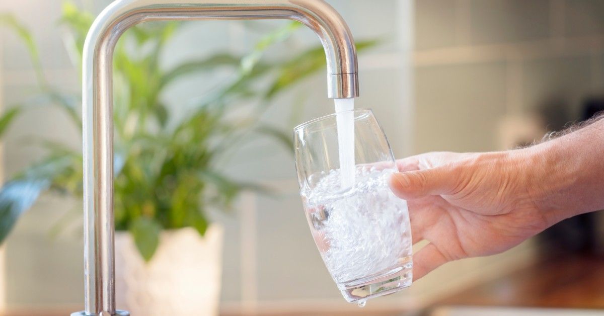 A hand holding a glass under a faucet on a wooden countertop, filling it with tap water.