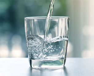 Water being poured into a clear glass on a bright table.