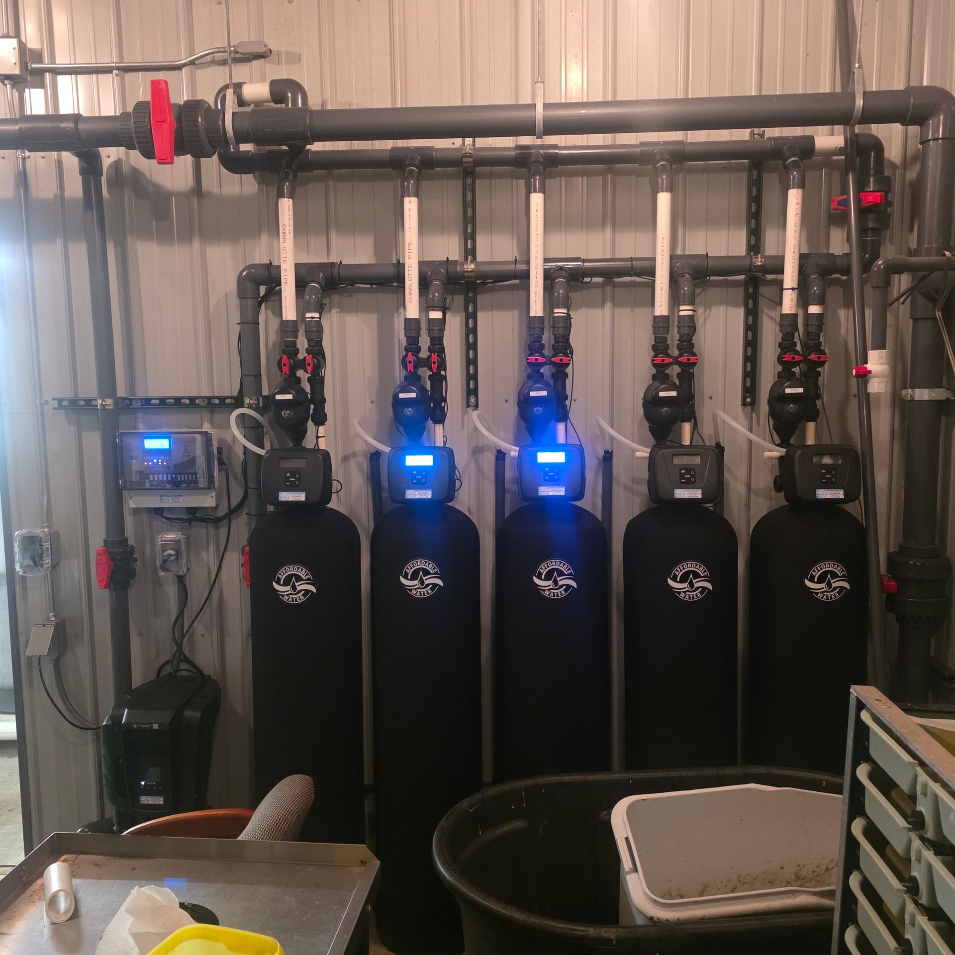 Row of black water filtration tanks with blue-lit control panels in a utility room