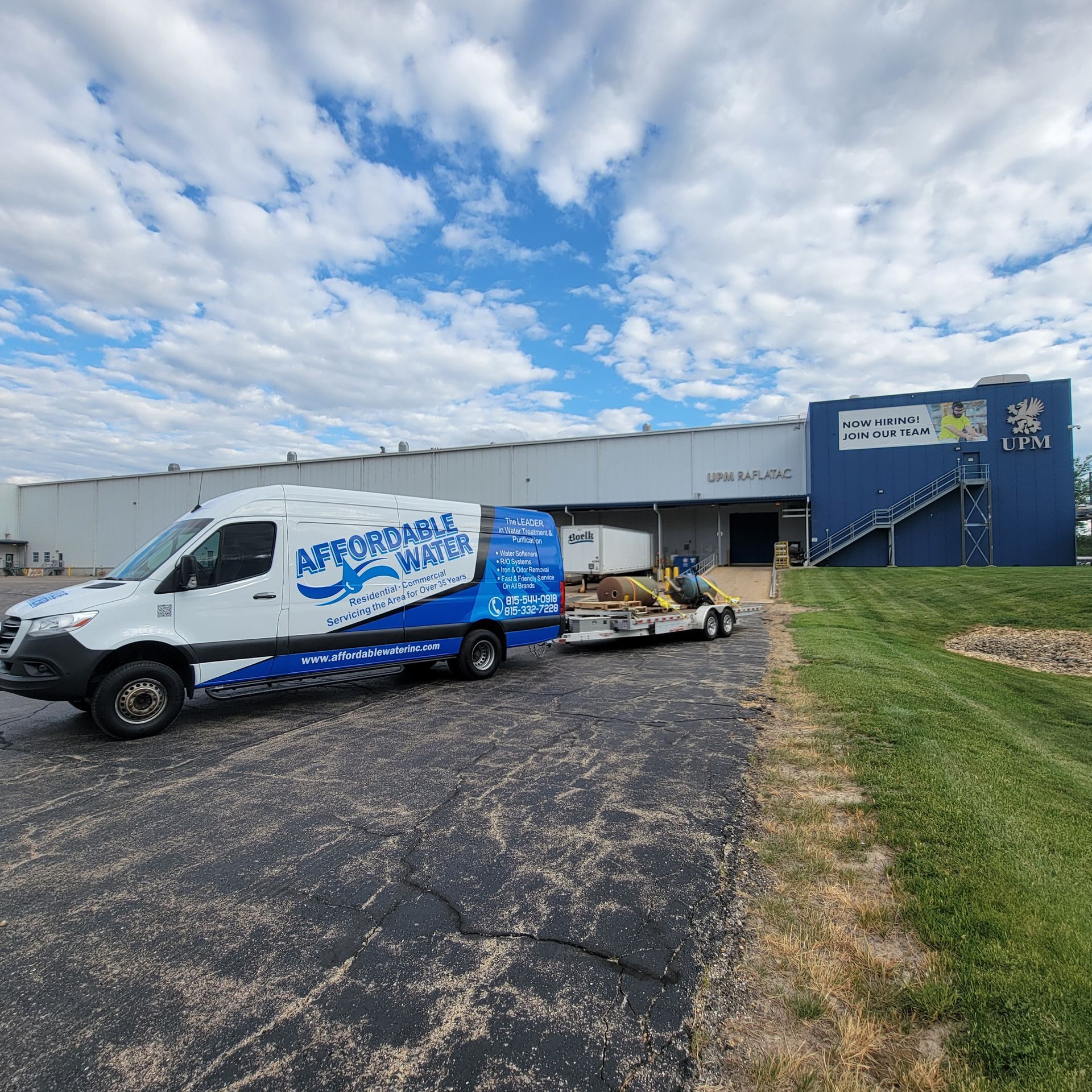 White service van and trailer parked beside a blue building under a cloudy sky