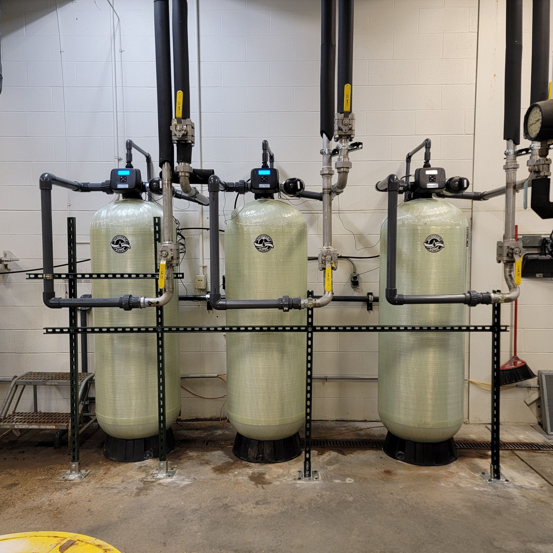 Three large beige industrial tanks with black piping and gauges in a utility room