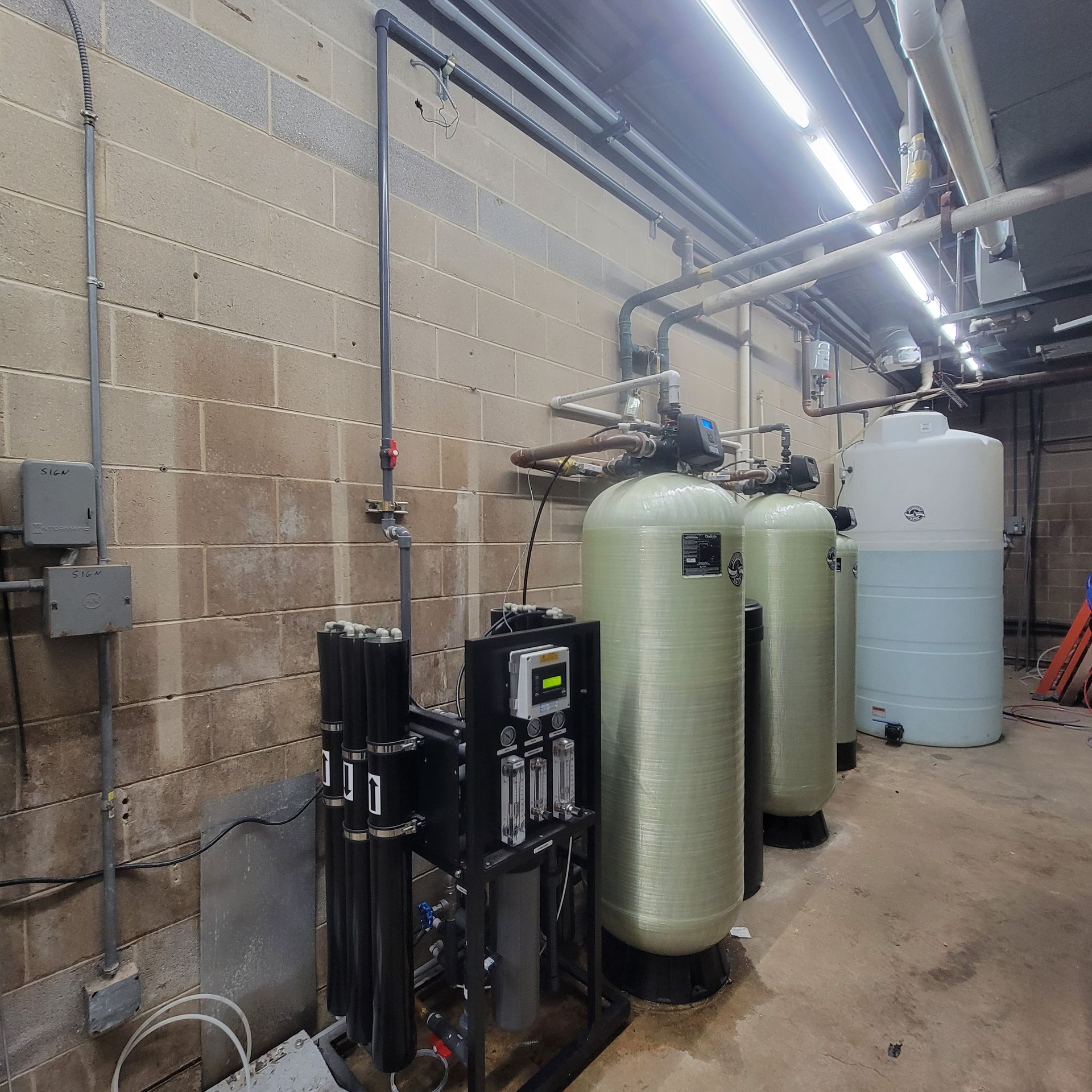 Industrial water treatment room with large tanks, pipes, and filtration equipment along a cinderblock wall