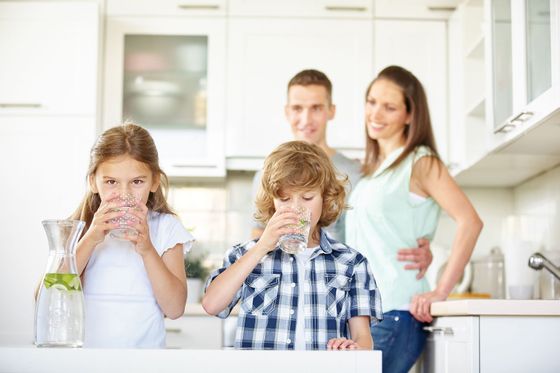 Children drinking from glasses while parents stand behind them