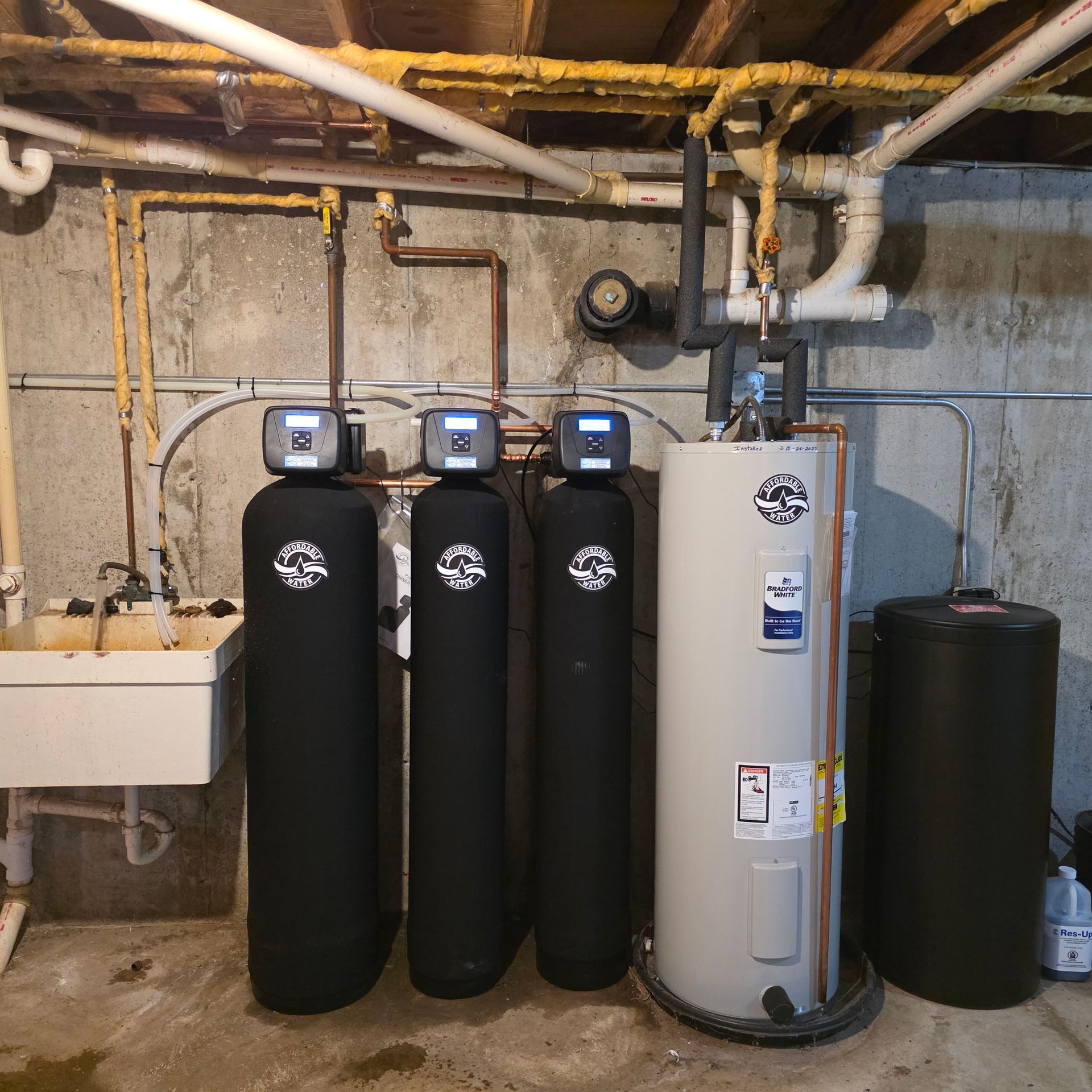 Water softener system with four black tanks and a tall white water heater in a basement utility room