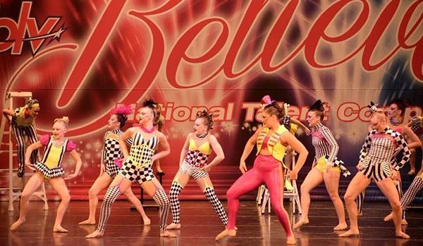 a group of young girls are dancing on a stage in front of a sign that says believe