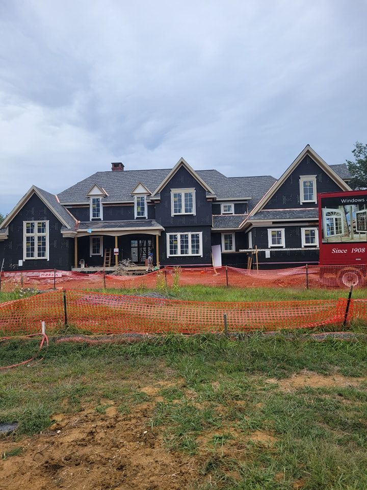 New home construction: dark siding, white trim, multiple gables, orange safety fencing, overcast sky.
