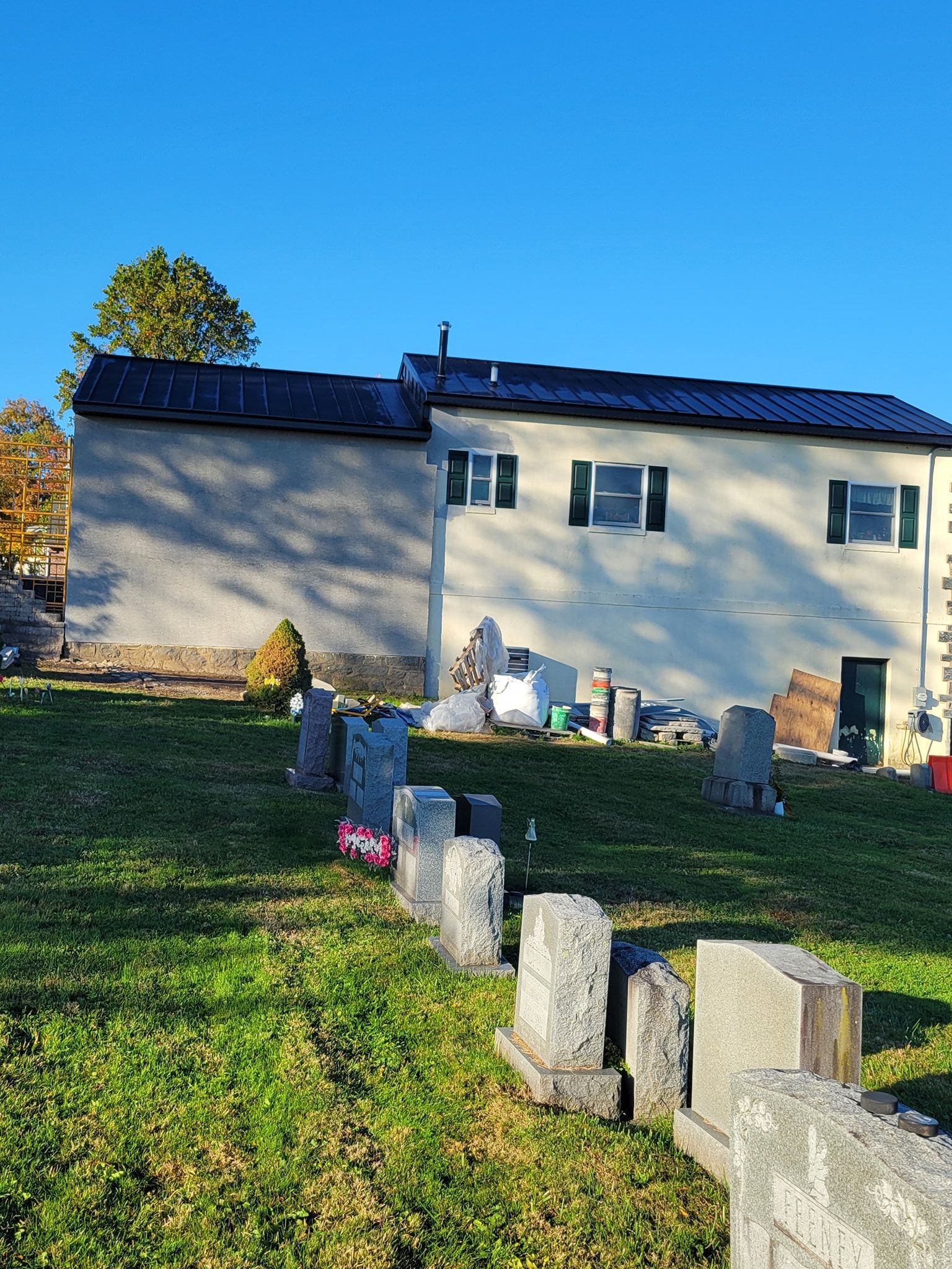 Row of old gravestones on a grassy hill, with a building in the background against a blue sky.