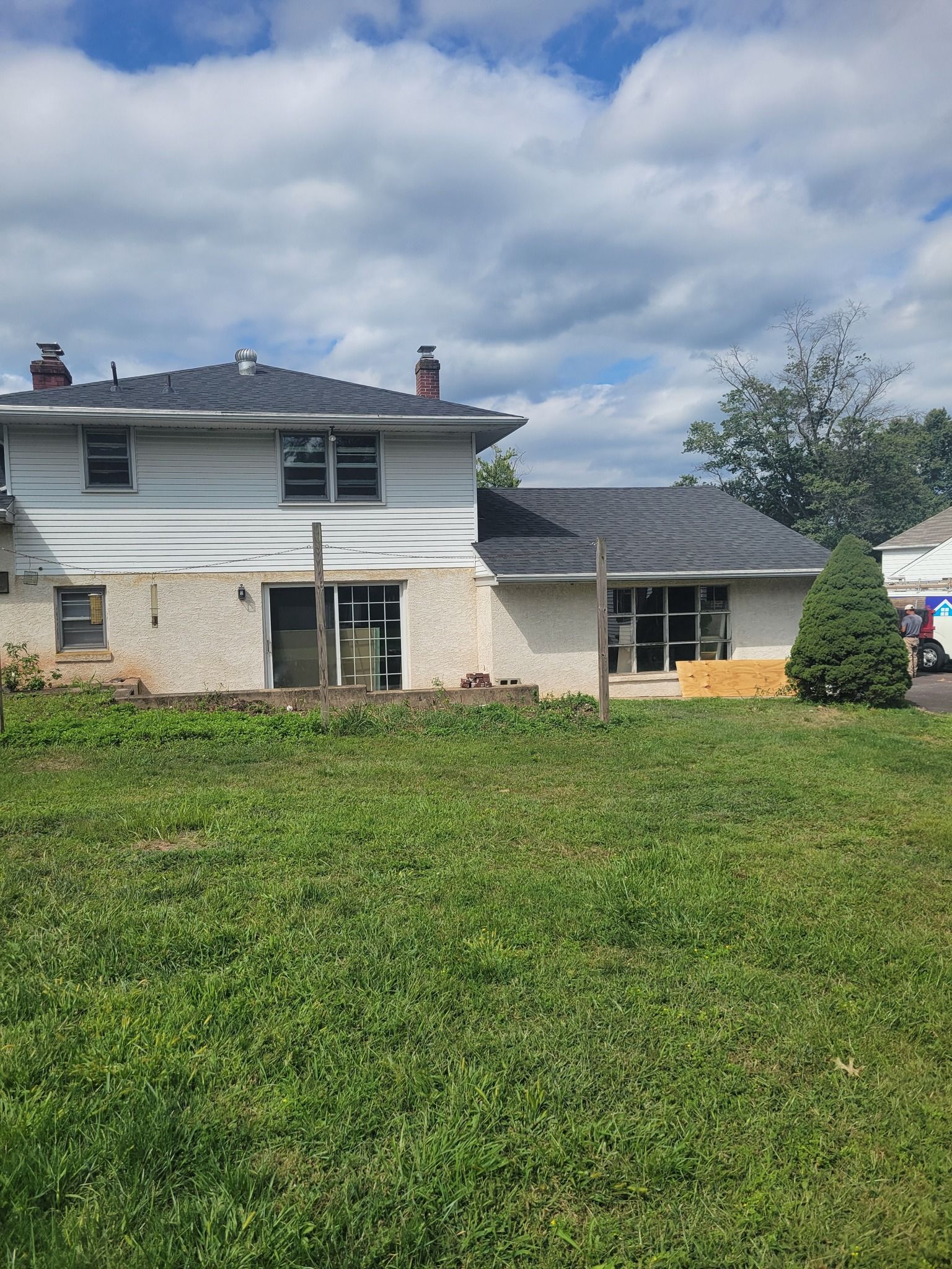 Rear view of a two-story house under construction with exposed walls and new roof. Green lawn in foreground.