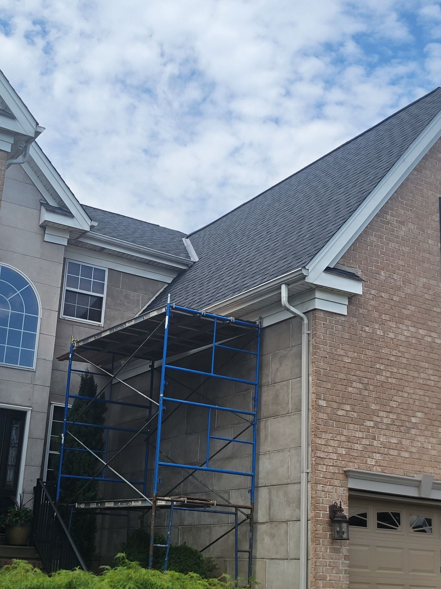 Scaffolding against a house with a gray roof and brick facade; blue sky in the background.