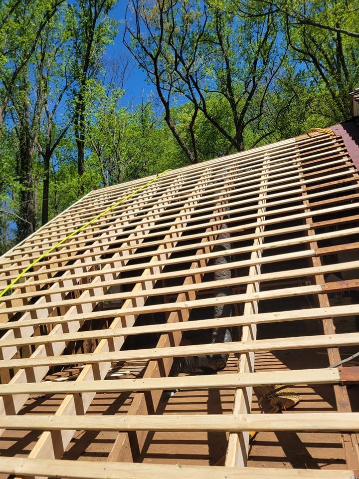 Wooden roof framework, outdoors, under construction with blue sky and green trees in the background.