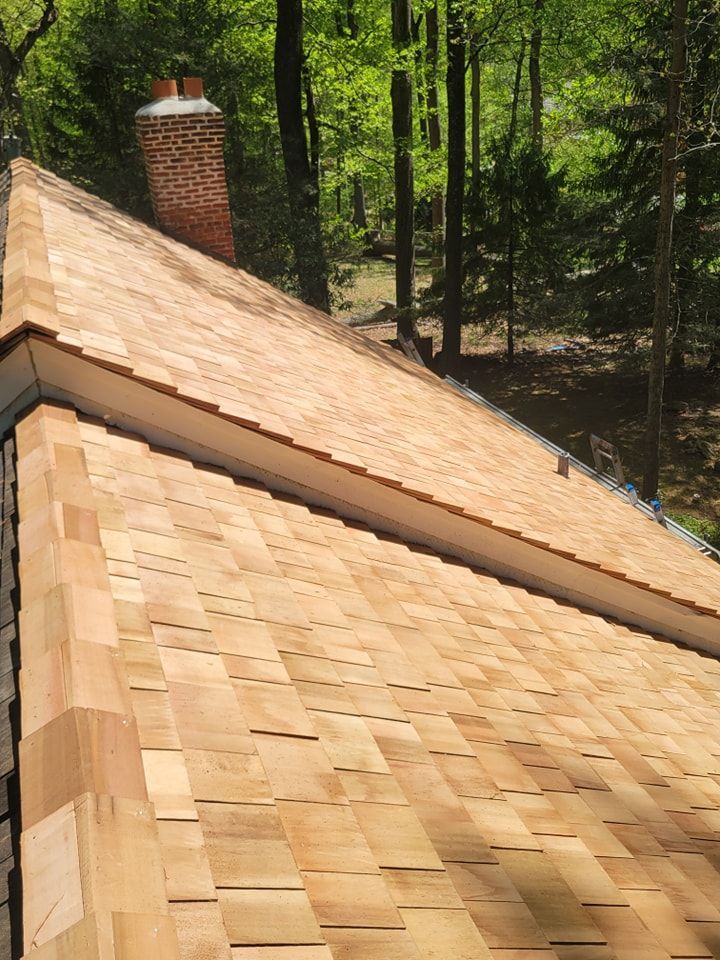 Wooden shingle roof with a brick chimney against a backdrop of trees.