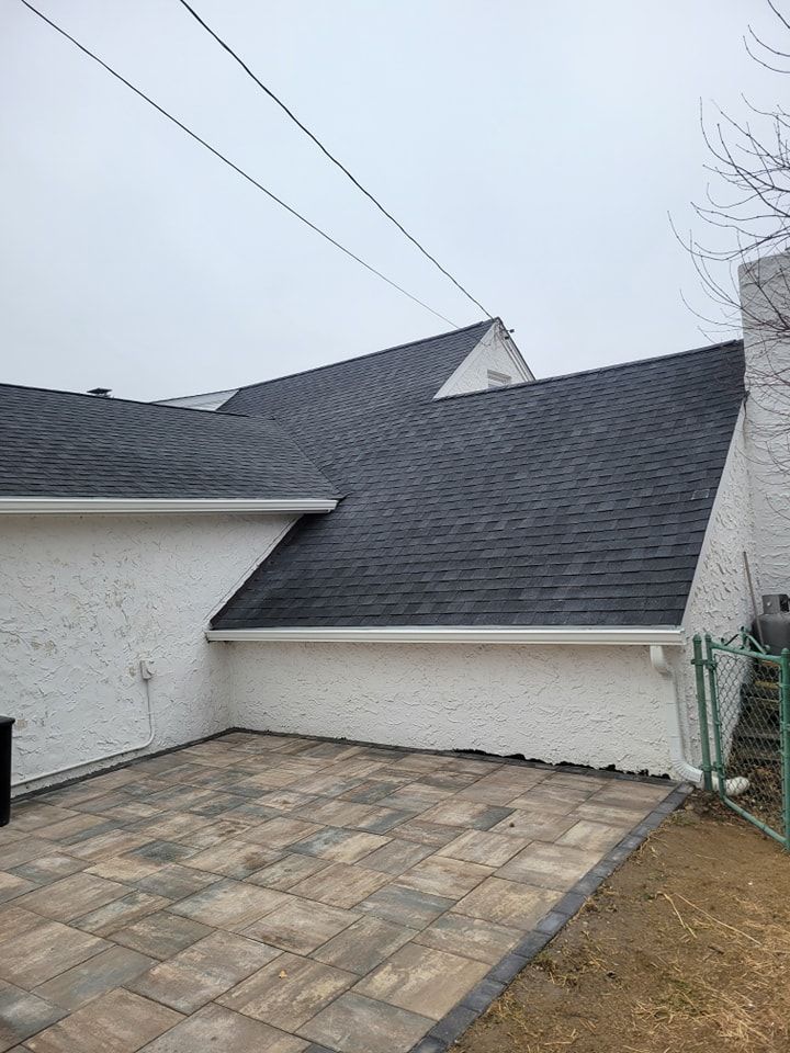 Exterior of a house with dark gray roof, white stucco walls, and a brick patio.