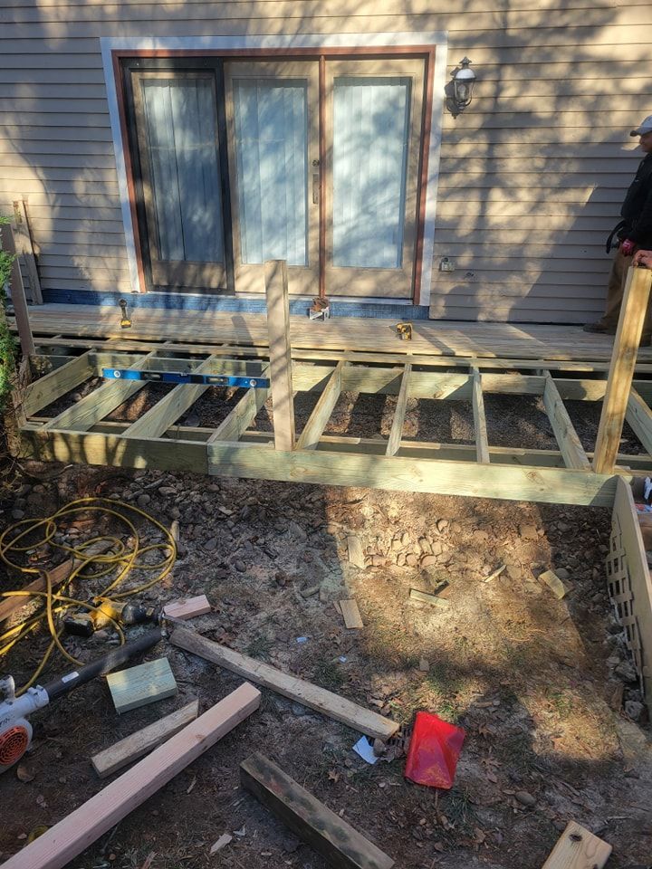 Deck under construction in front of a sliding glass door. Lumber, tools, and a person are visible.