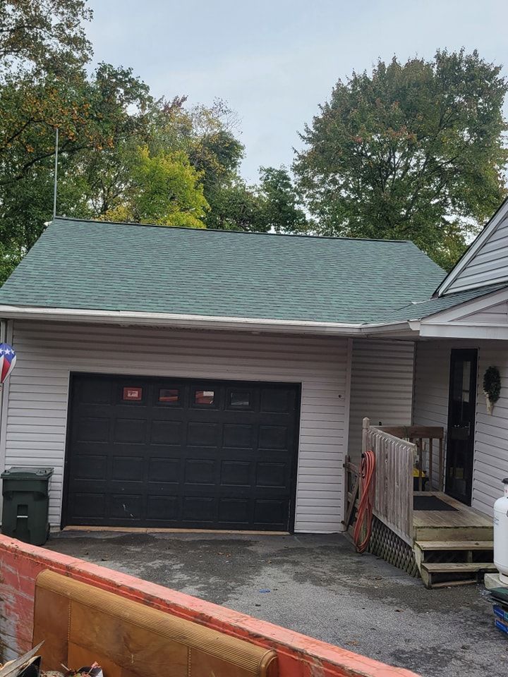 Garage with black door, green roof, and light-colored siding. Gray overcast sky.